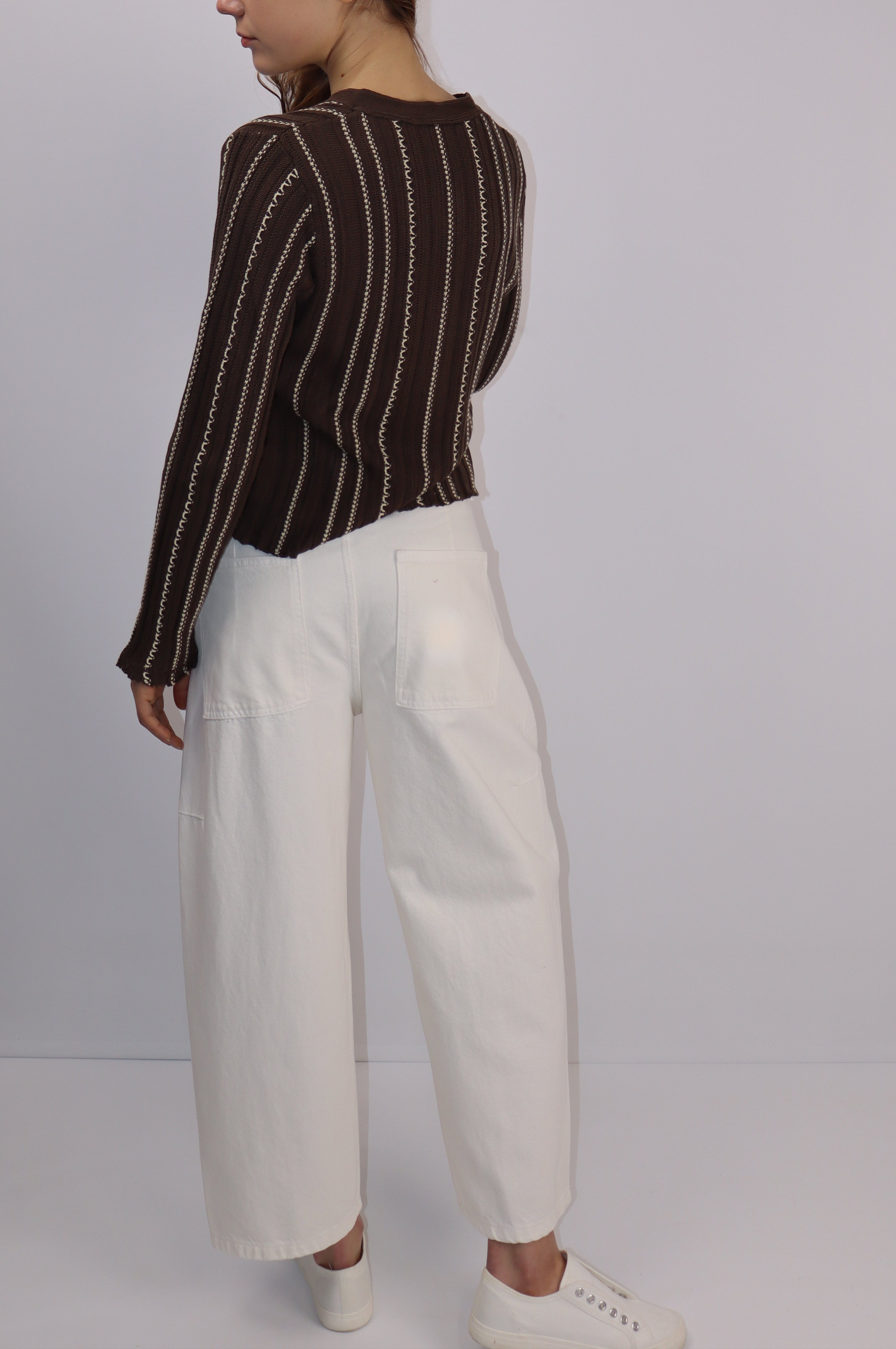 Person wearing a brown striped sweater and white pants on a plain background