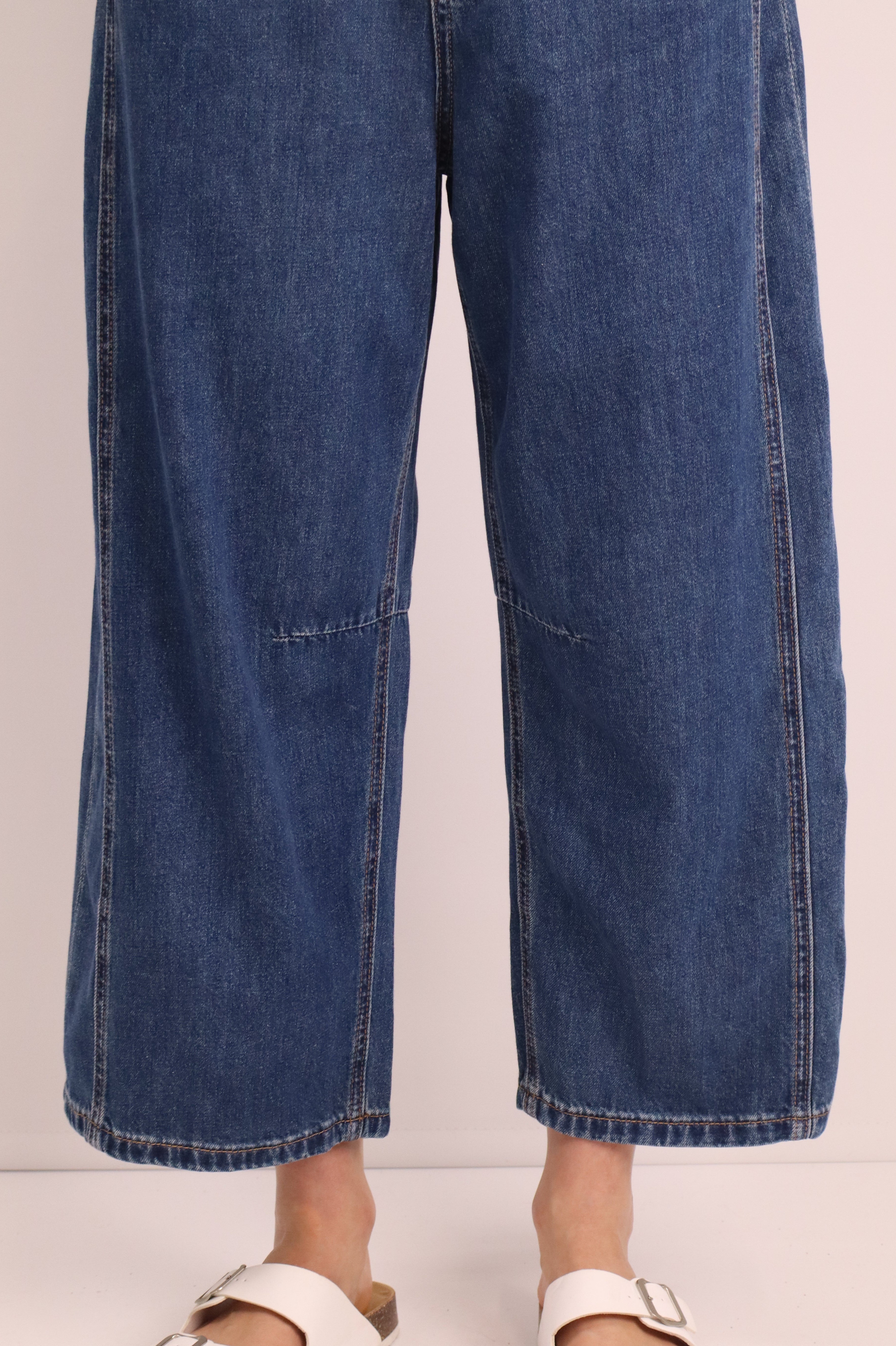 Blue jeans being worn with white sandals on a light background