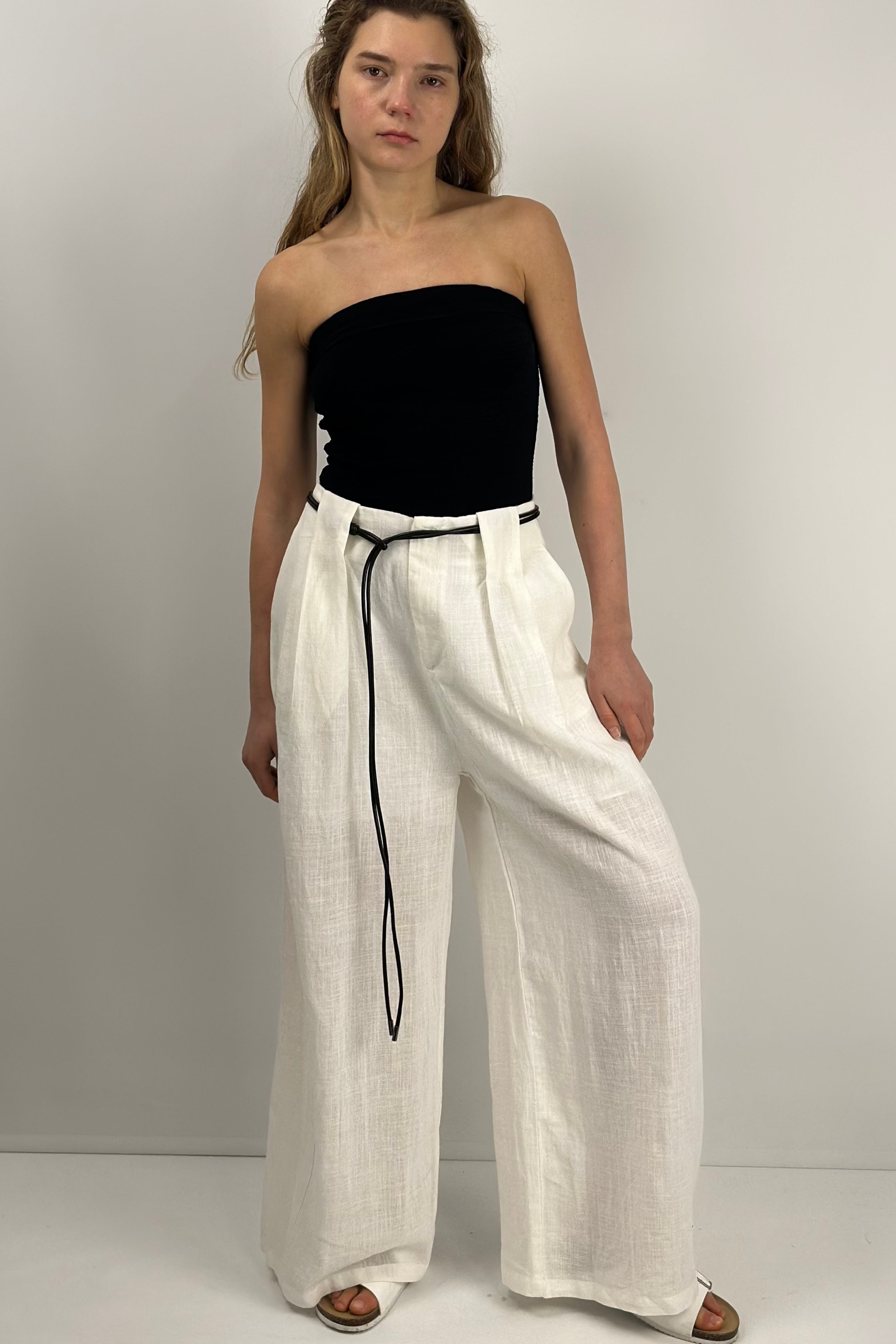 Woman wearing a black strapless top and white wide-leg pants on a plain background