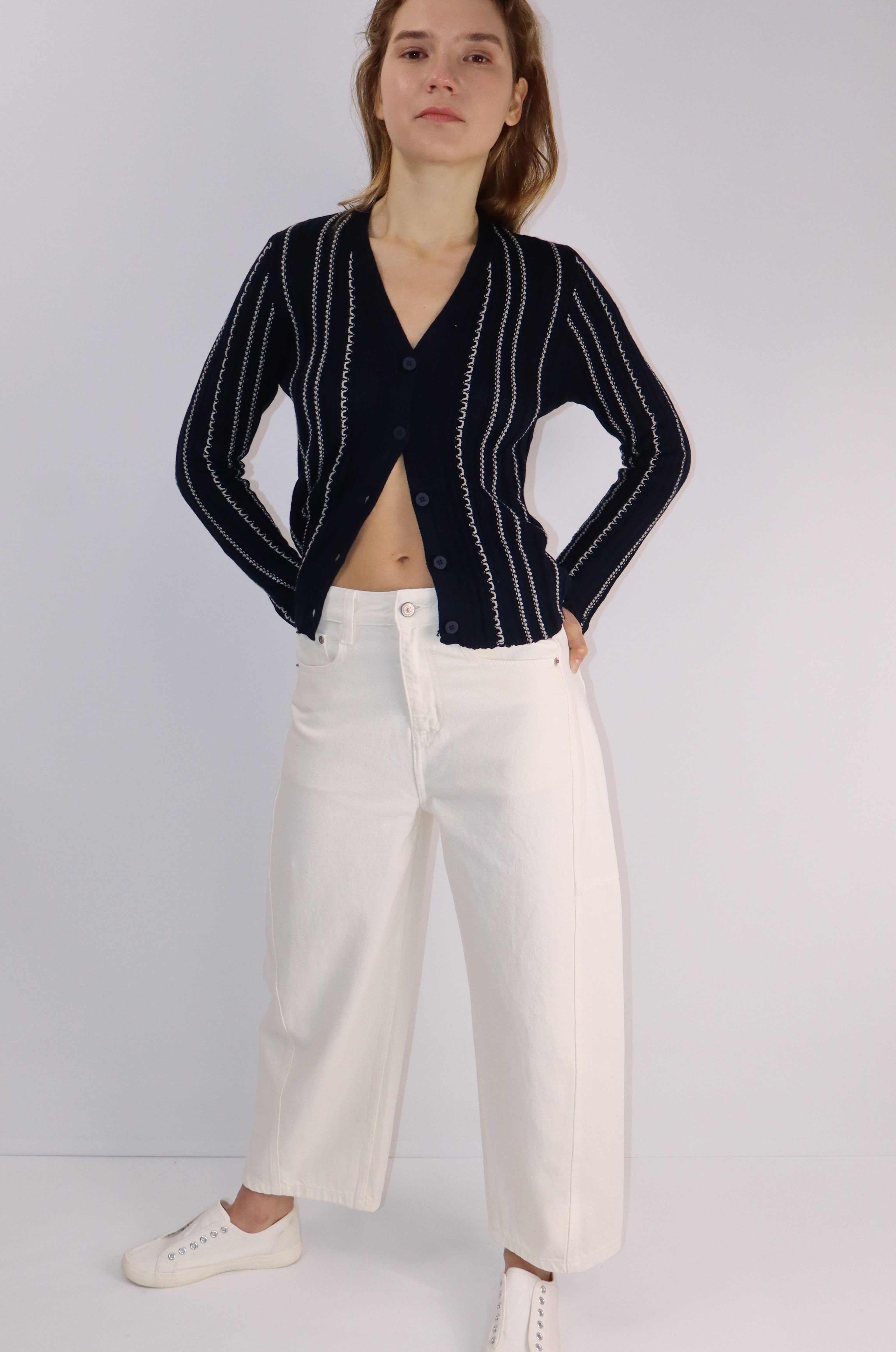 Person wearing a black pinstripe blazer and white pants on a plain background