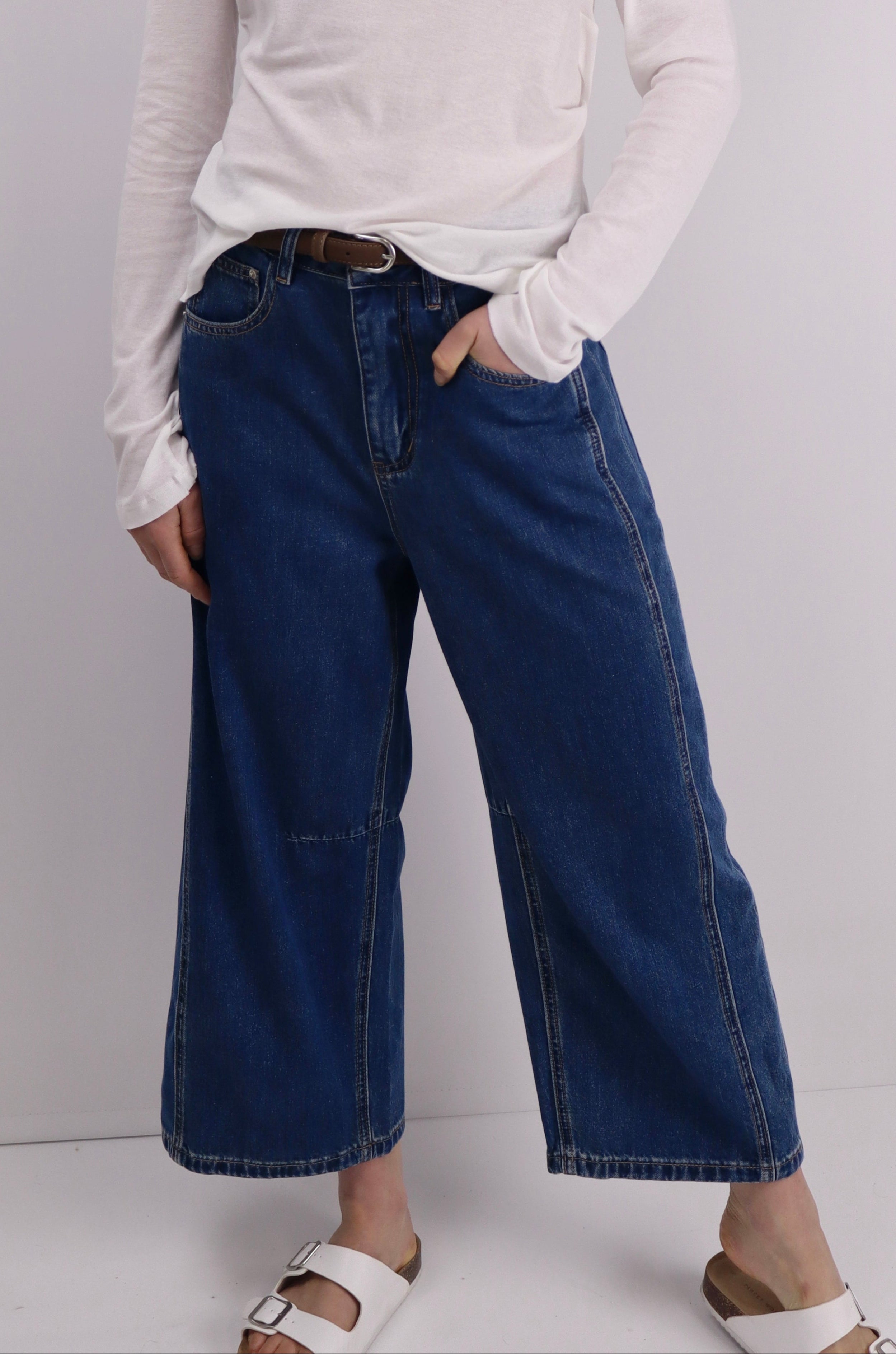 Person wearing a white long-sleeve shirt and blue cropped jeans against a plain background