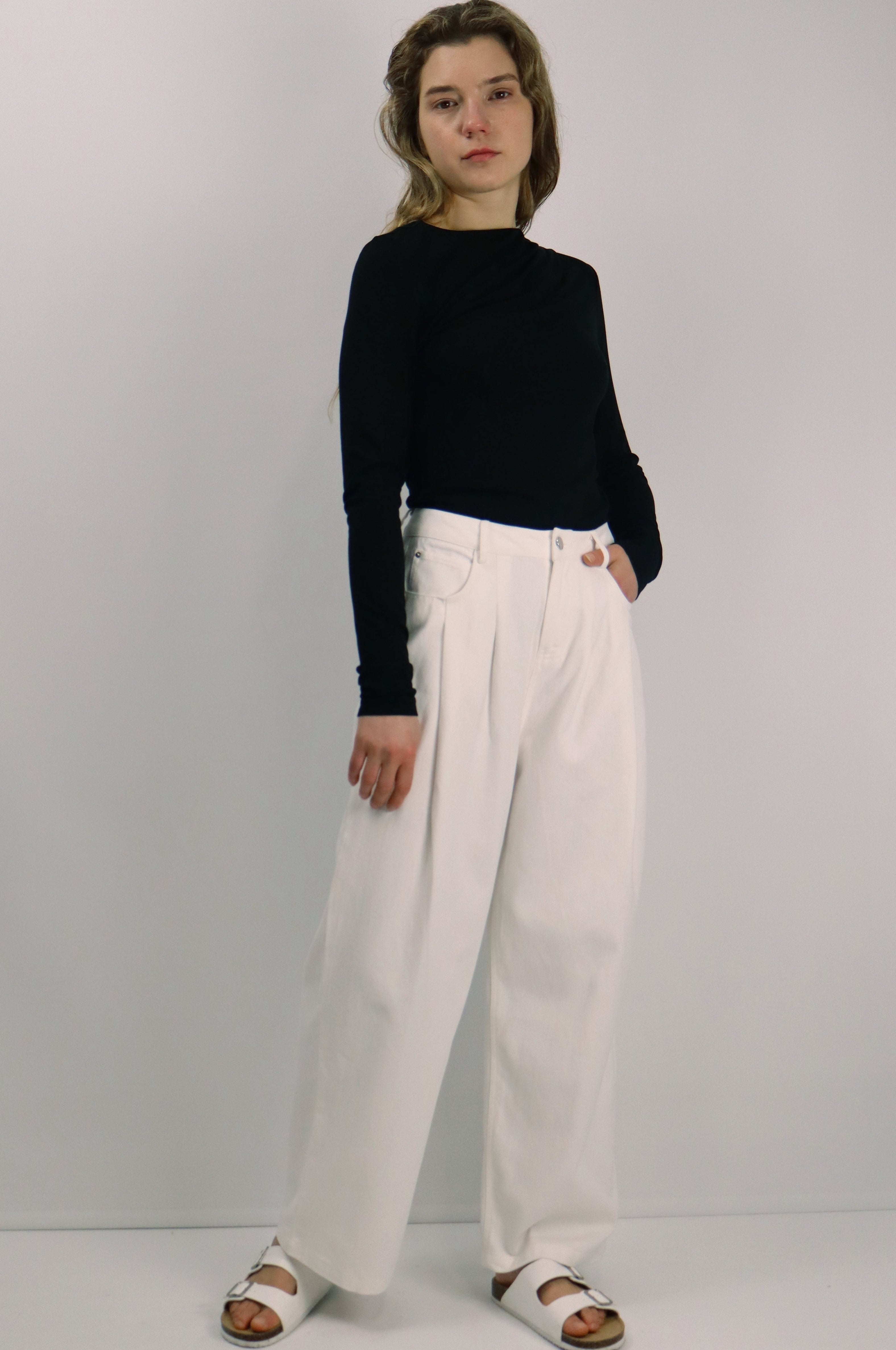 Person wearing a black sweater and white pants against a plain background