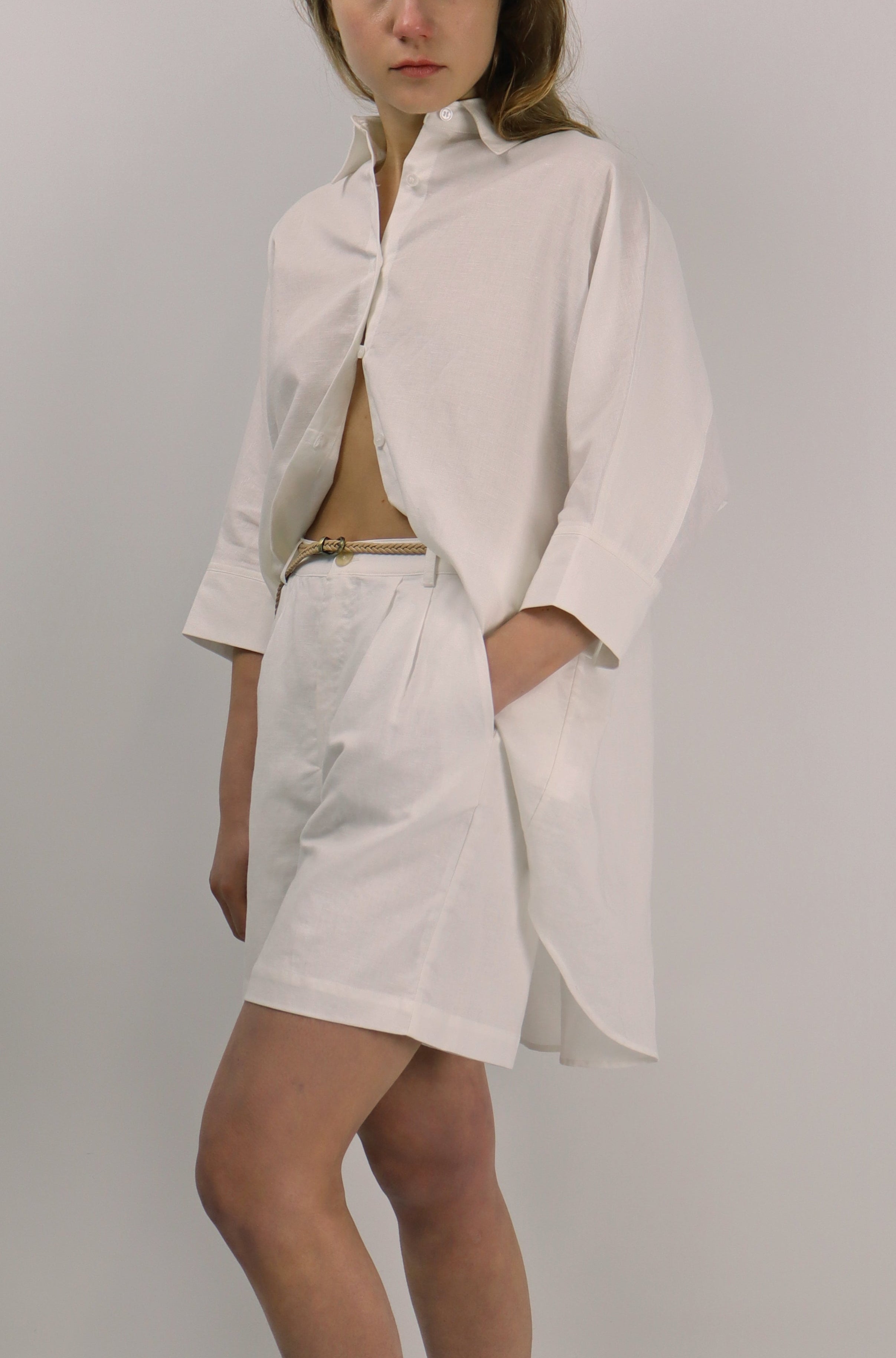 Woman wearing a white linen outfit with a jacket and skirt on a plain background