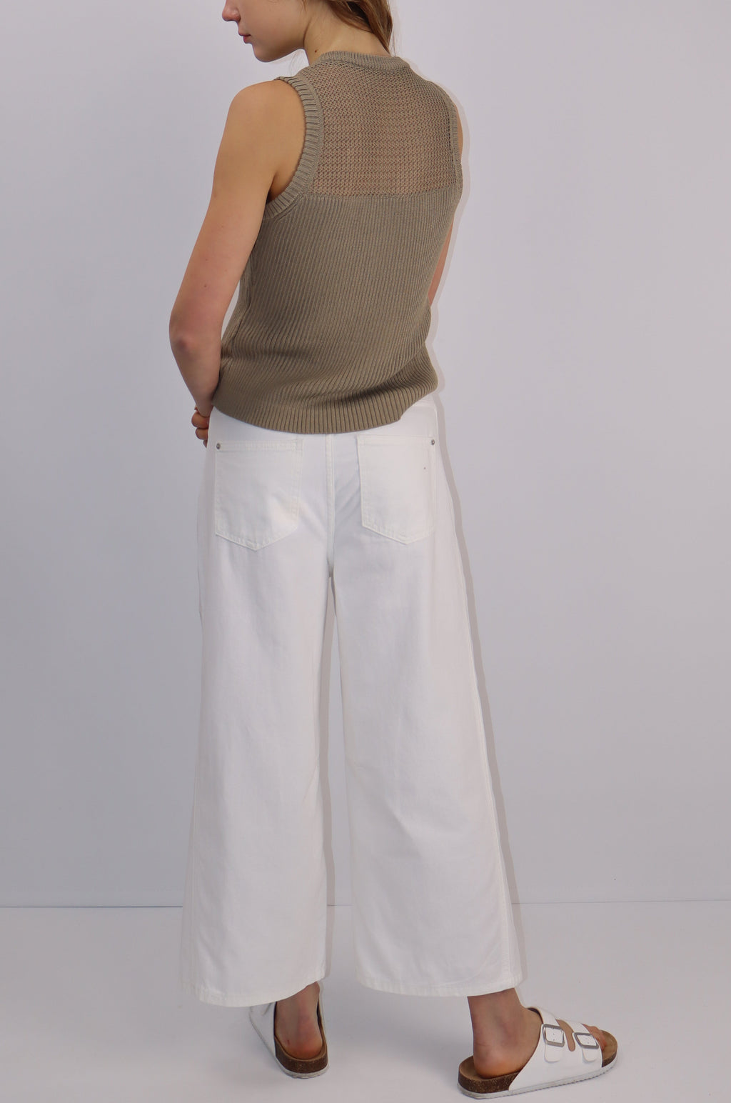 Person wearing a green top and white pants against a plain background