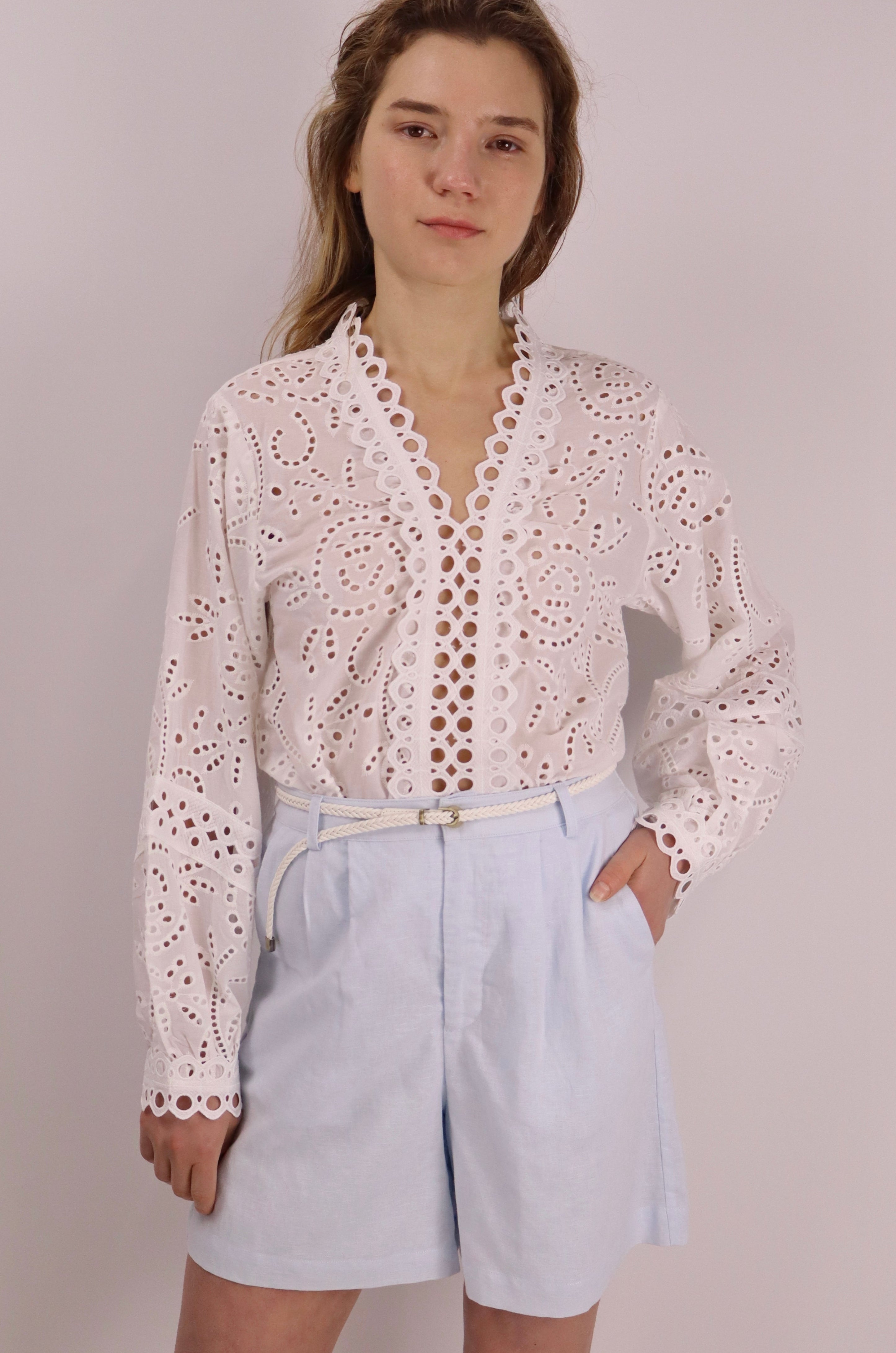 Woman wearing a white lace blouse and light blue shorts against a plain background
