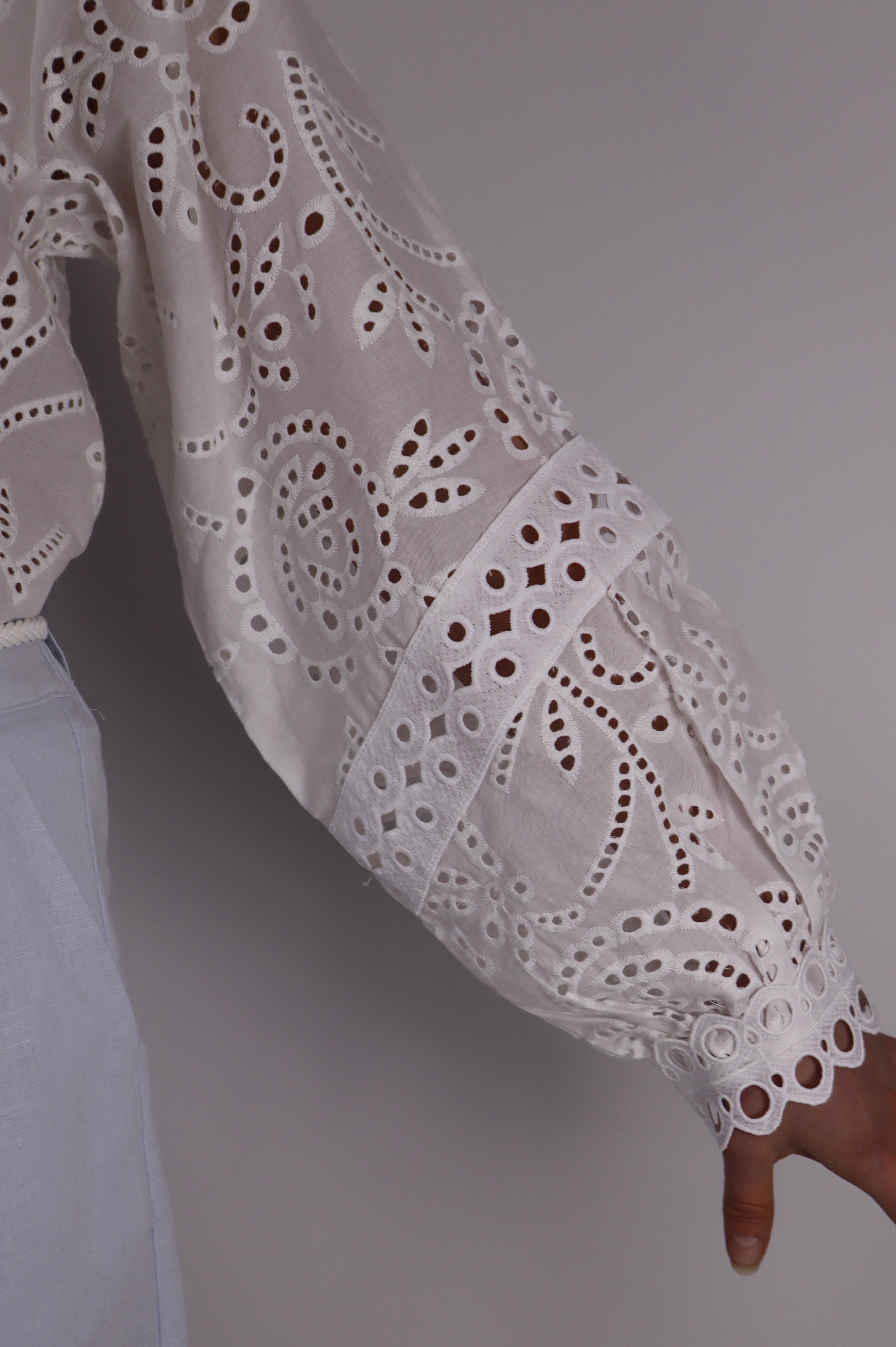 Close-up of a person wearing a white lace sleeve against a gray background