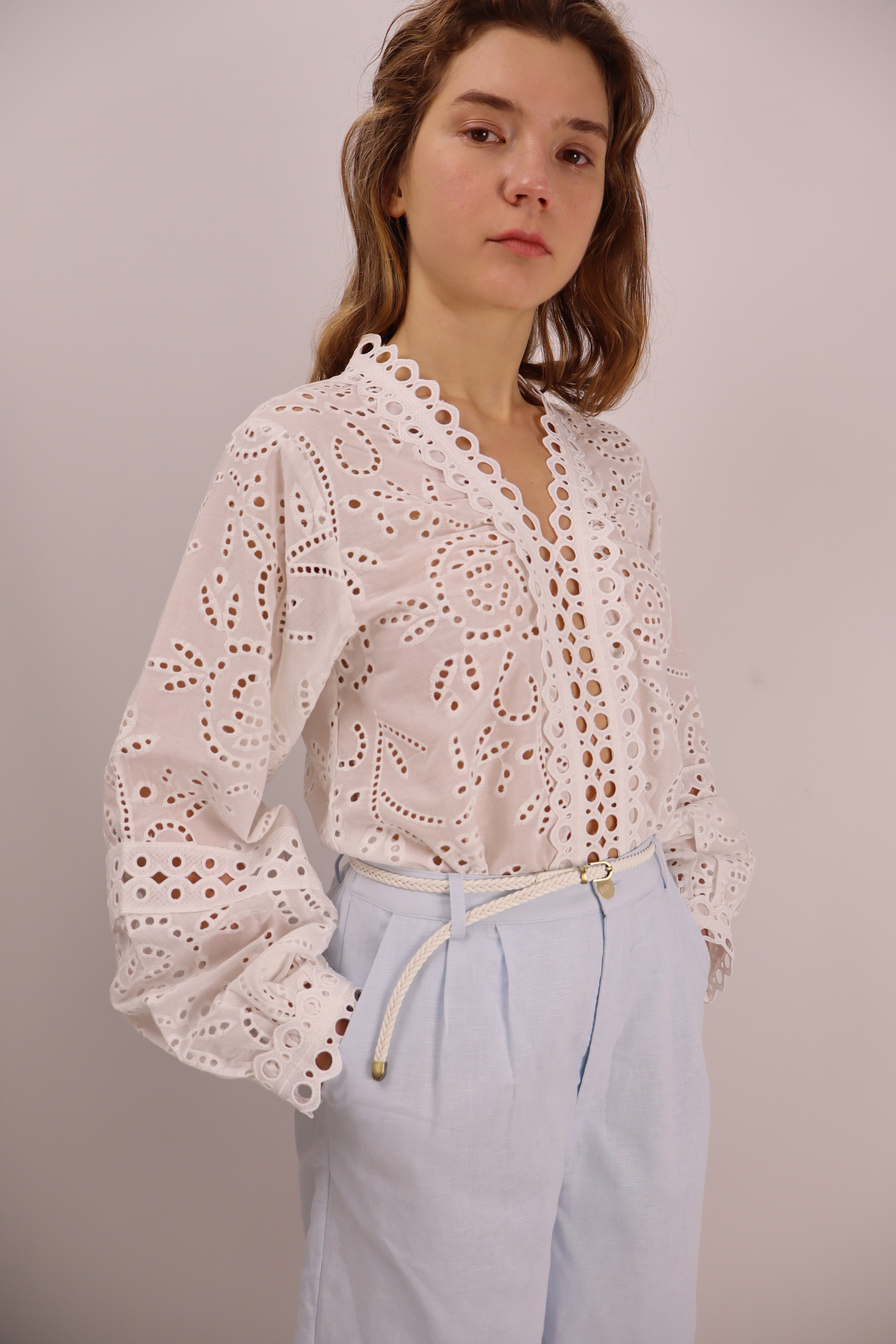 Woman wearing a white lace top and light blue pants on a plain background