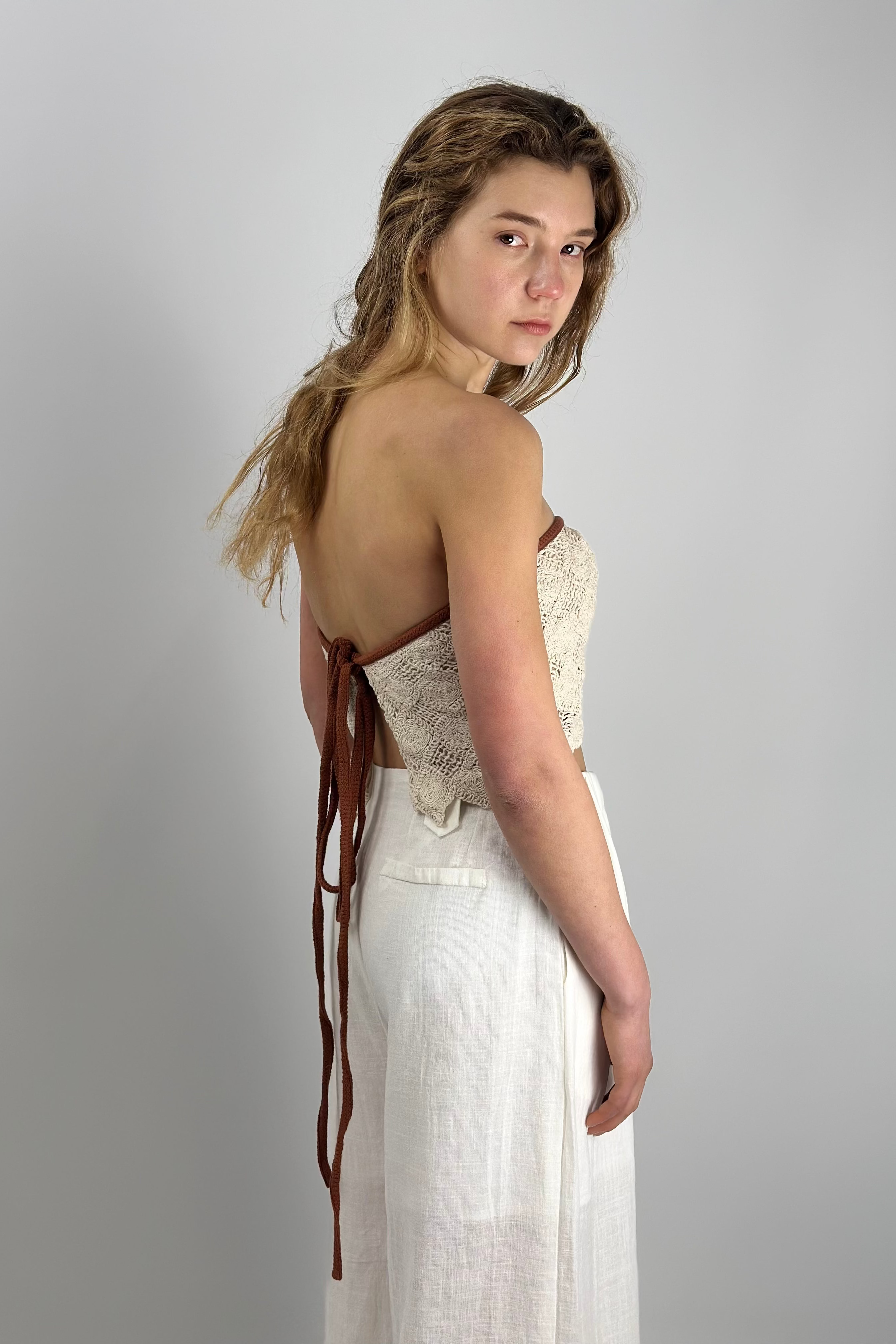 Model wearing 100% cotton crochet tie-back top with open back and linen trousers