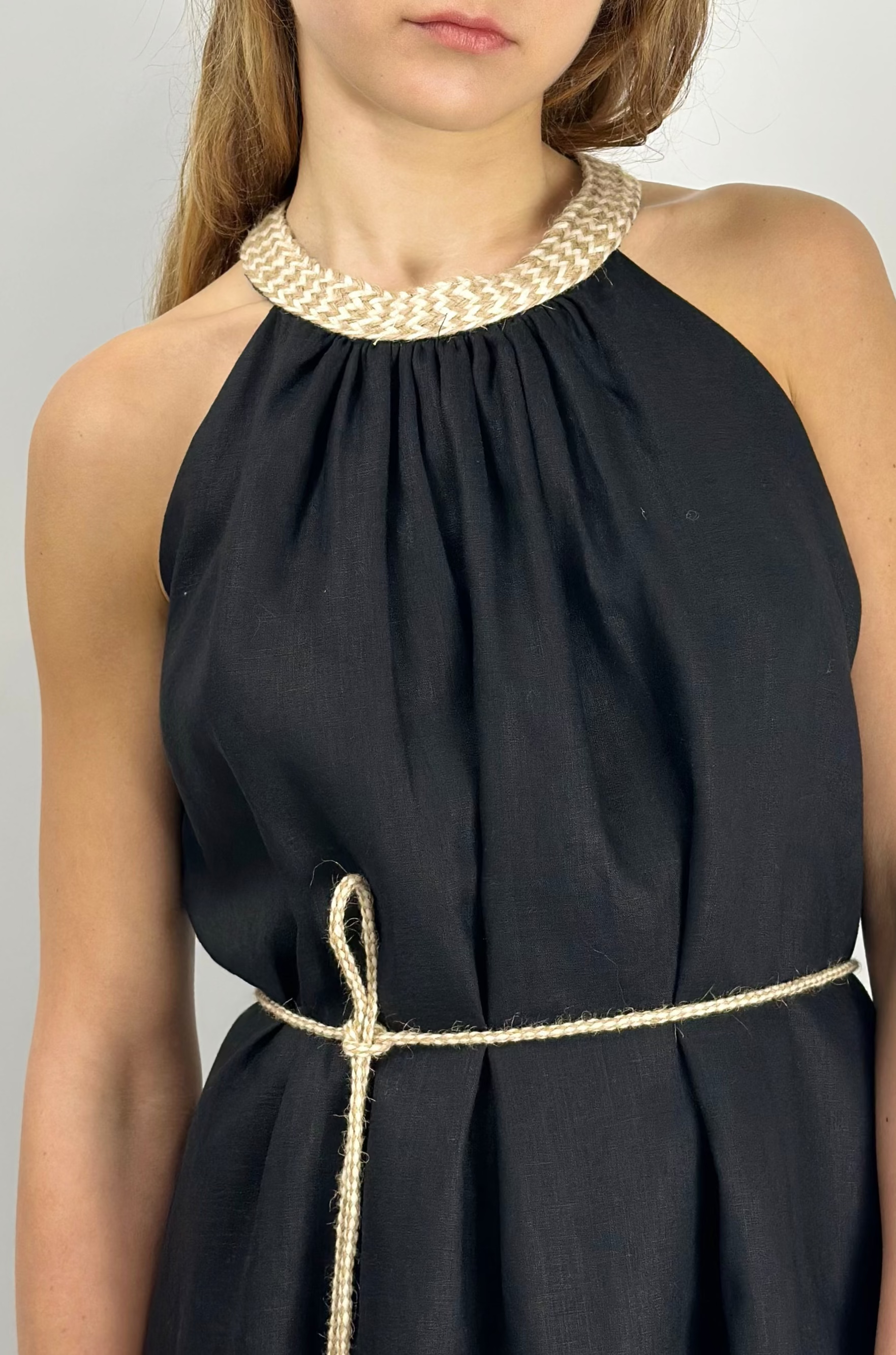 Woman wearing a black halter neck linen dress with a white background