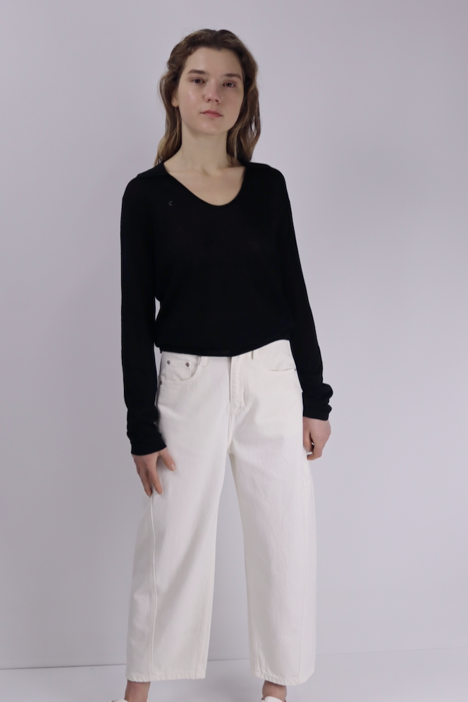 Person wearing a black linen sweater and white pants on a plain background