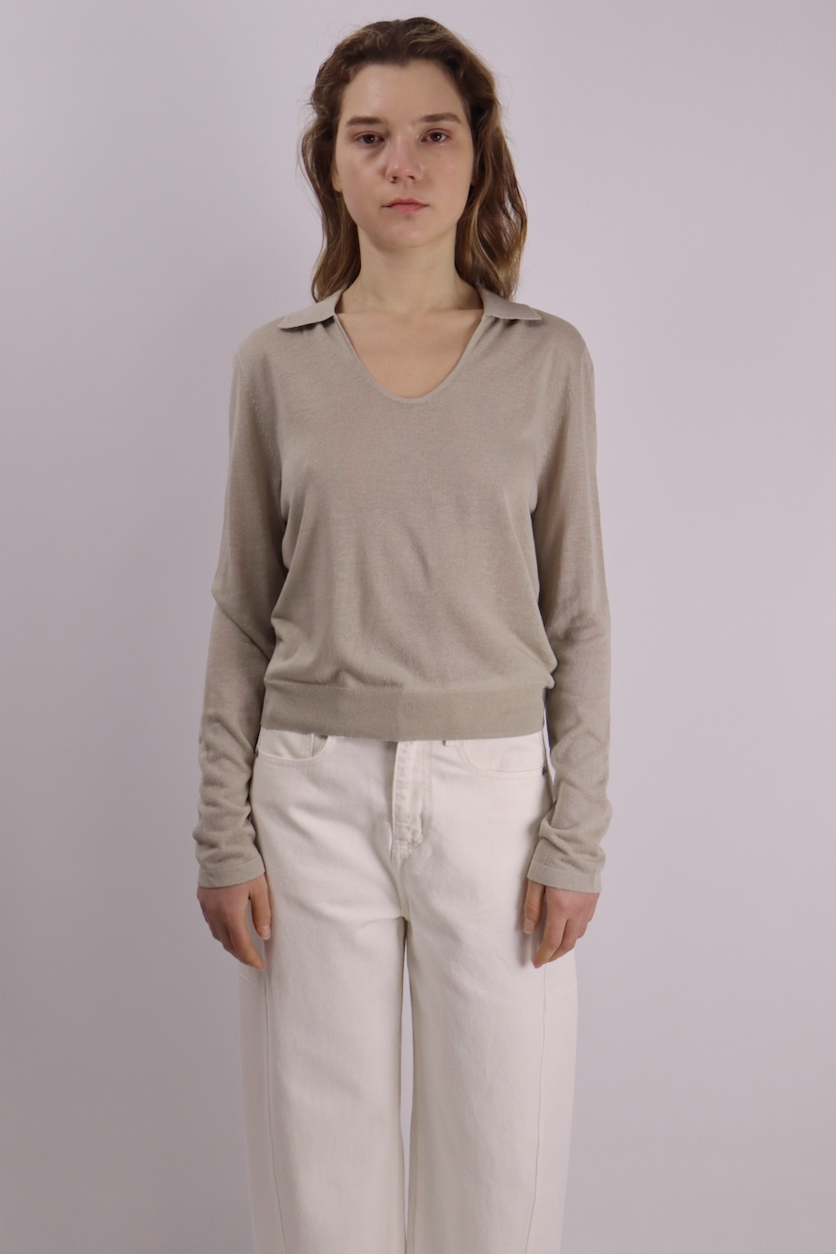 Person wearing a beige linen sweater and white pants against a plain background
