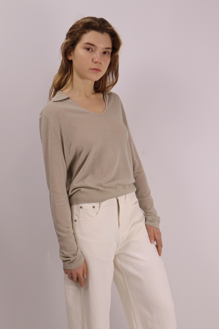 Woman wearing a beige long-sleeve top and white pants against a plain background