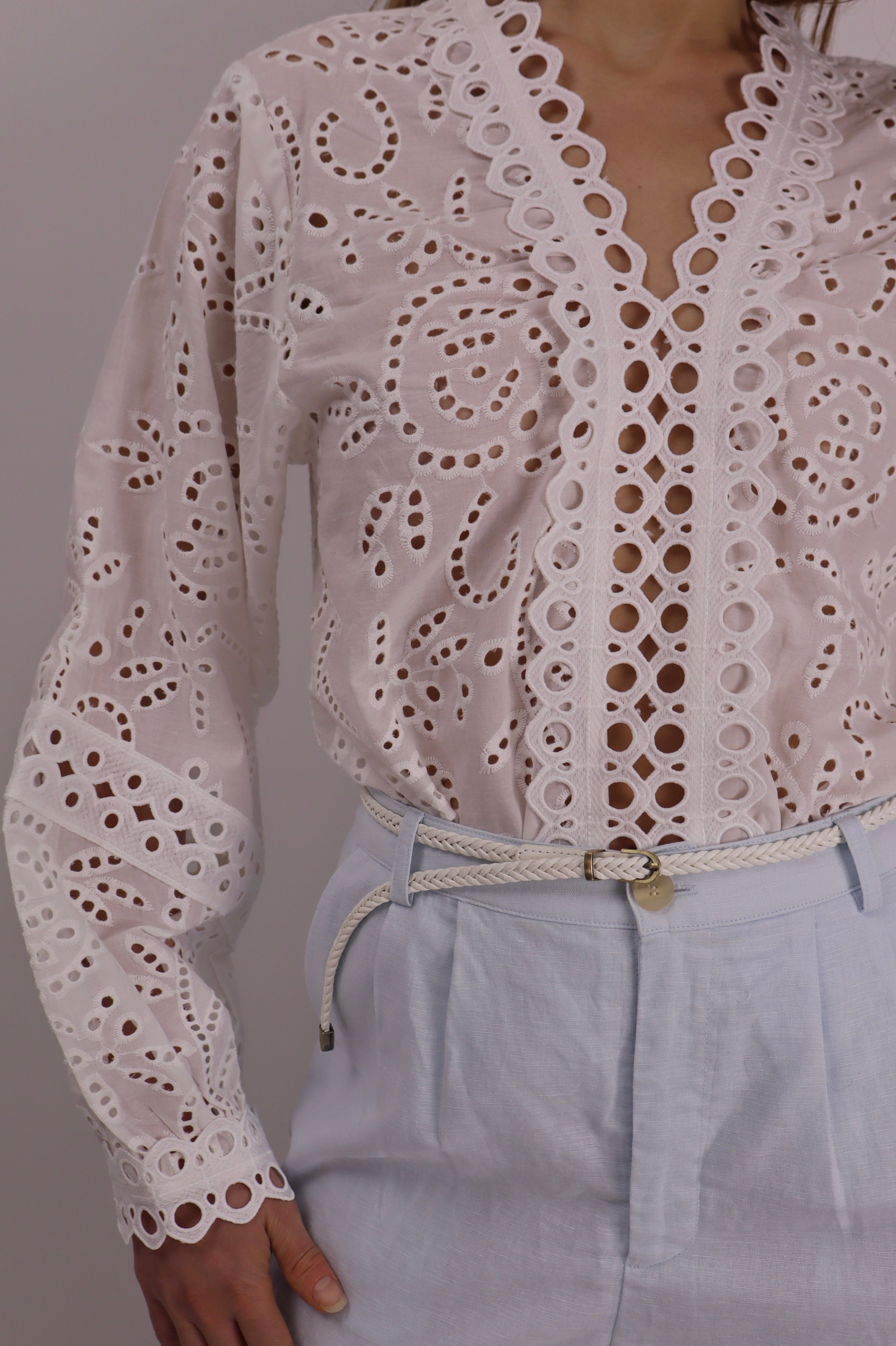 White lace top with long sleeves and light blue pants on a plain background