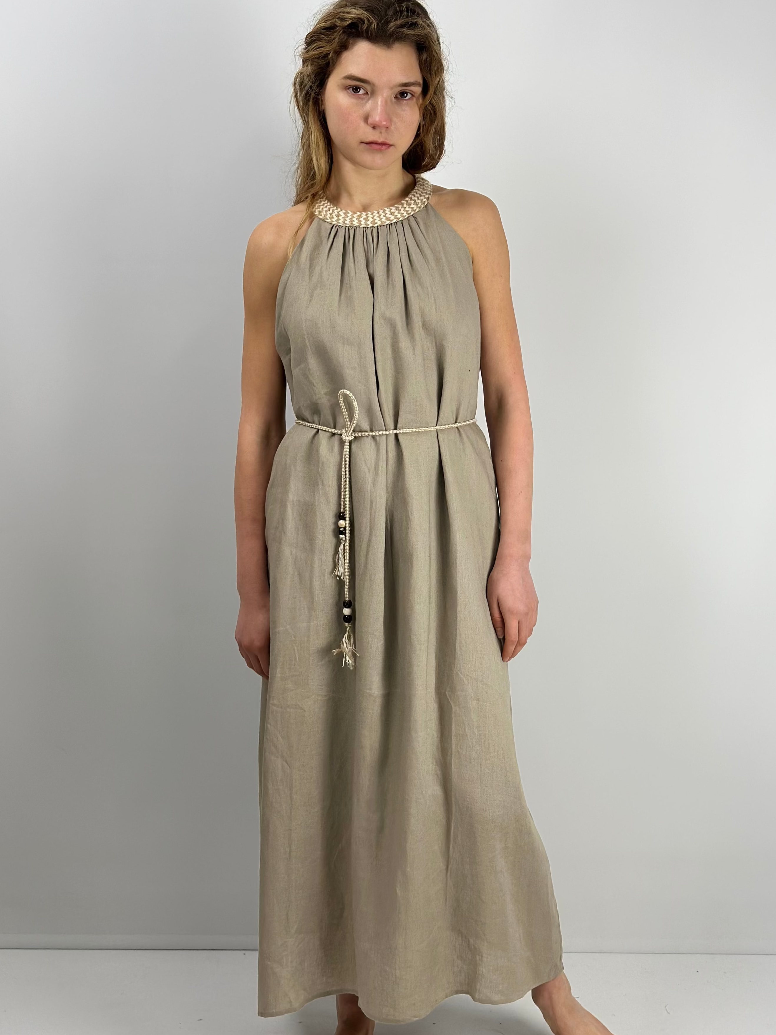 Woman wearing a maxi linen sleeveless dress with a belt against a plain background