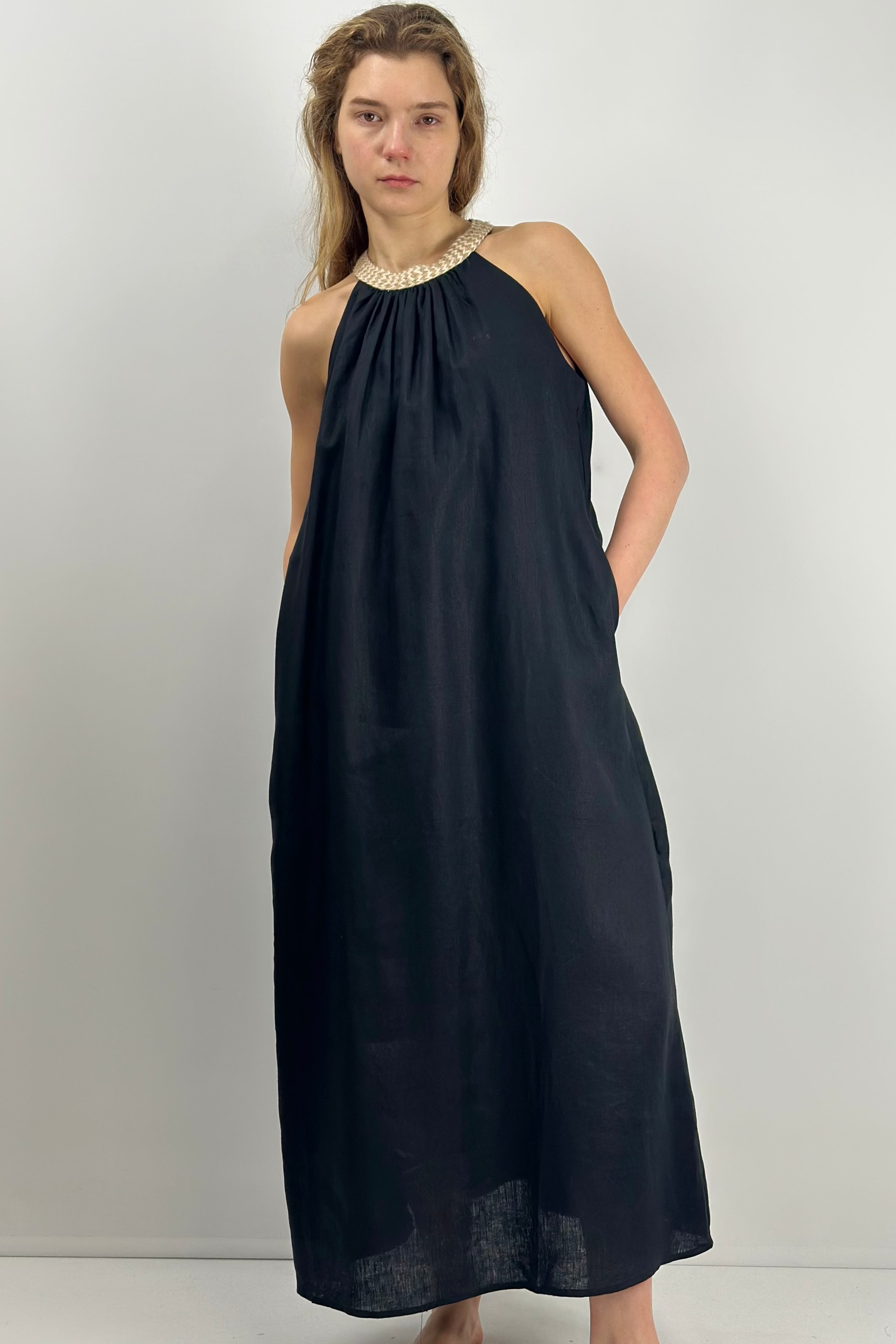 Woman wearing a black sleeveless linen dress with a gold neckline against a white background