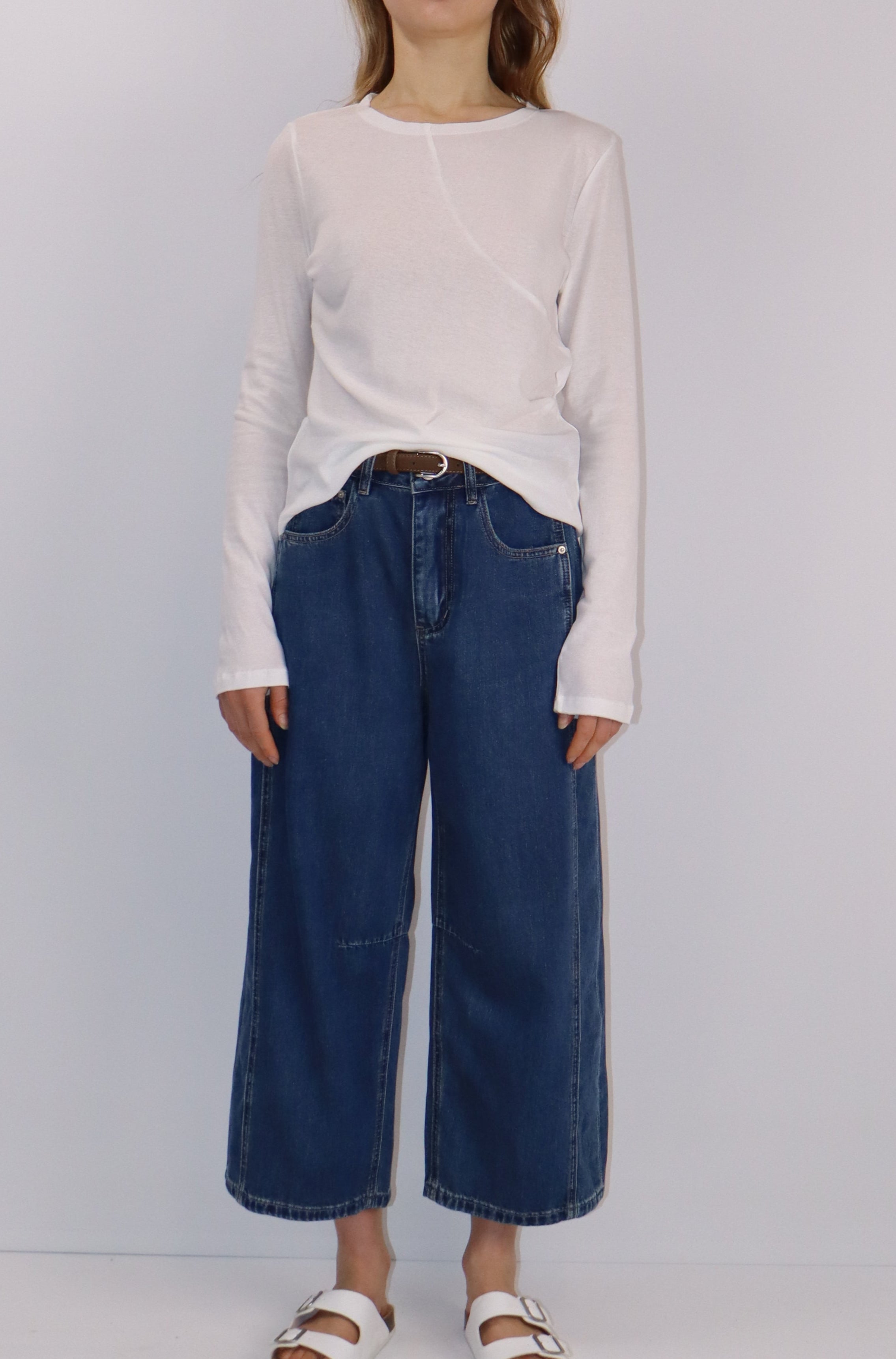 Person wearing a white shirt and blue cropped blue jeans standing on a white background