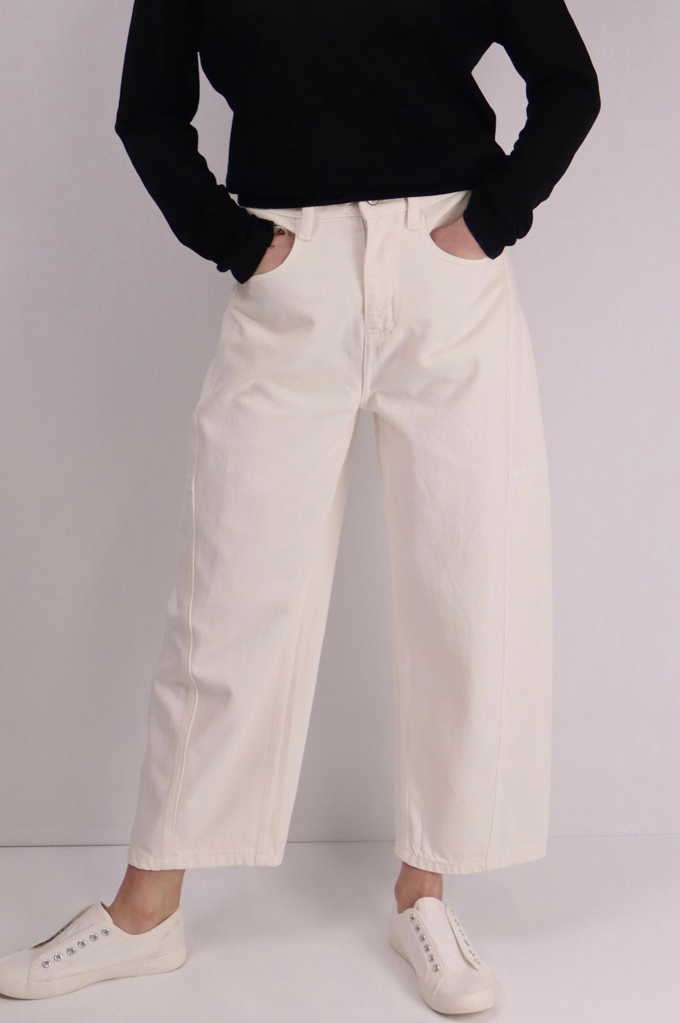 Alt text：
Model wearing mid-rise, curved-leg white cotton pants paired with a black long-sleeve top and white slip-on sneakers, standing against a plain light background.