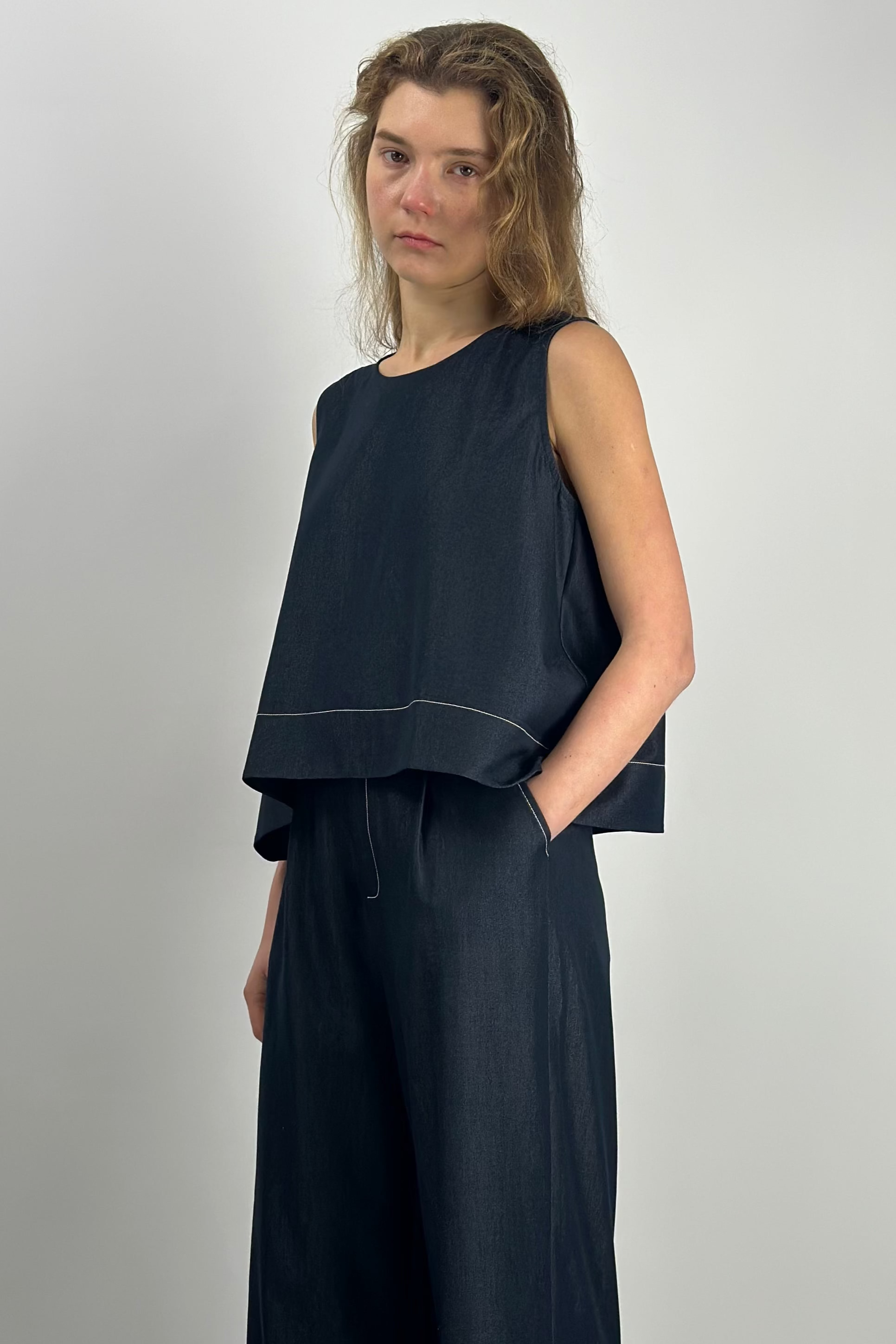 Woman wearing a dark blue sleeveless top and wide-leg pants on a plain background