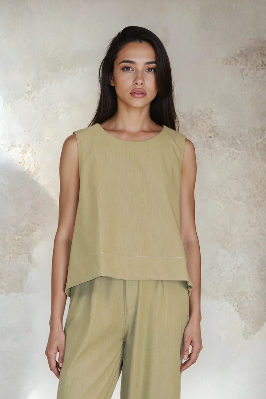 Woman wearing a green sleeveless top and wide-leg pants against a textured wall.