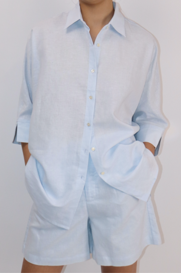Model wearing oversized baby blue linen-cotton shirt with button-down front and relaxed silhouette.