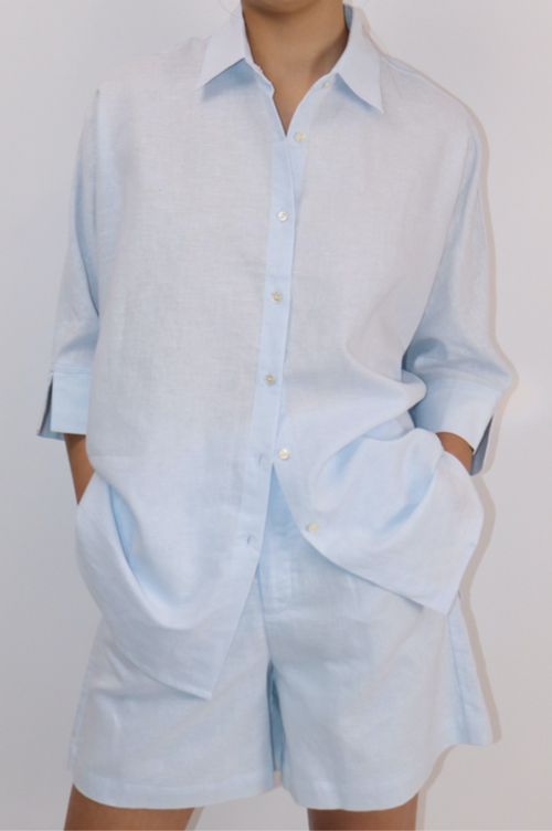 Model wearing oversized baby blue linen-cotton shirt with button-down front and relaxed silhouette.