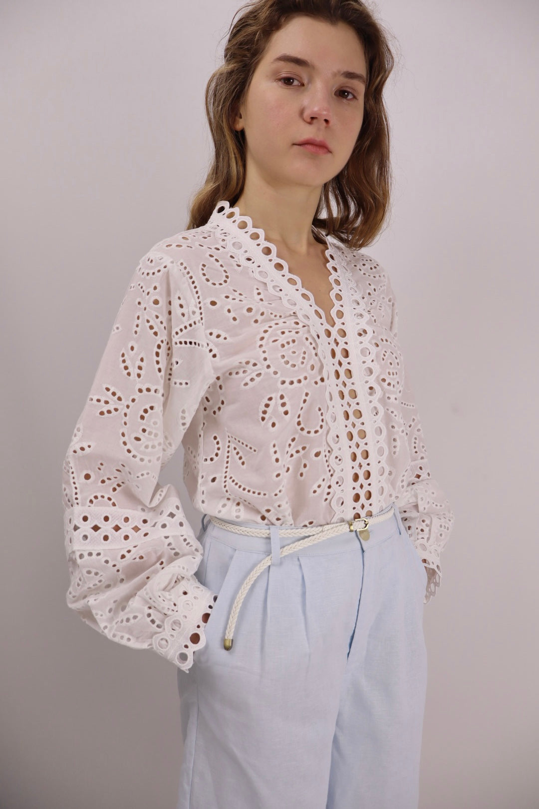 Model wearing a white cotton eyelet blouse with scalloped edges and long sleeves, paired with light blue shorts.