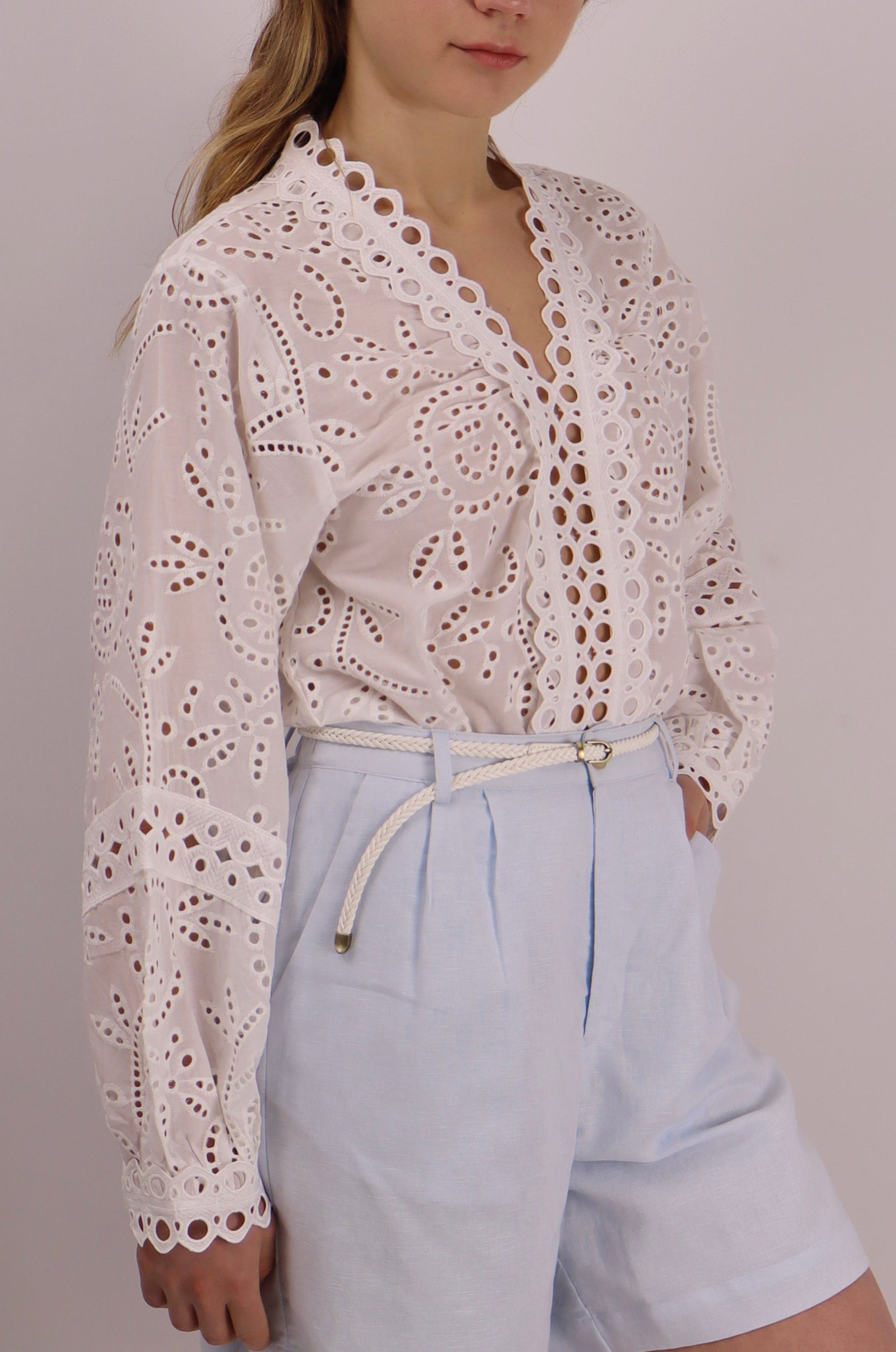 Woman wearing a white lace top and light blue shorts against a plain background