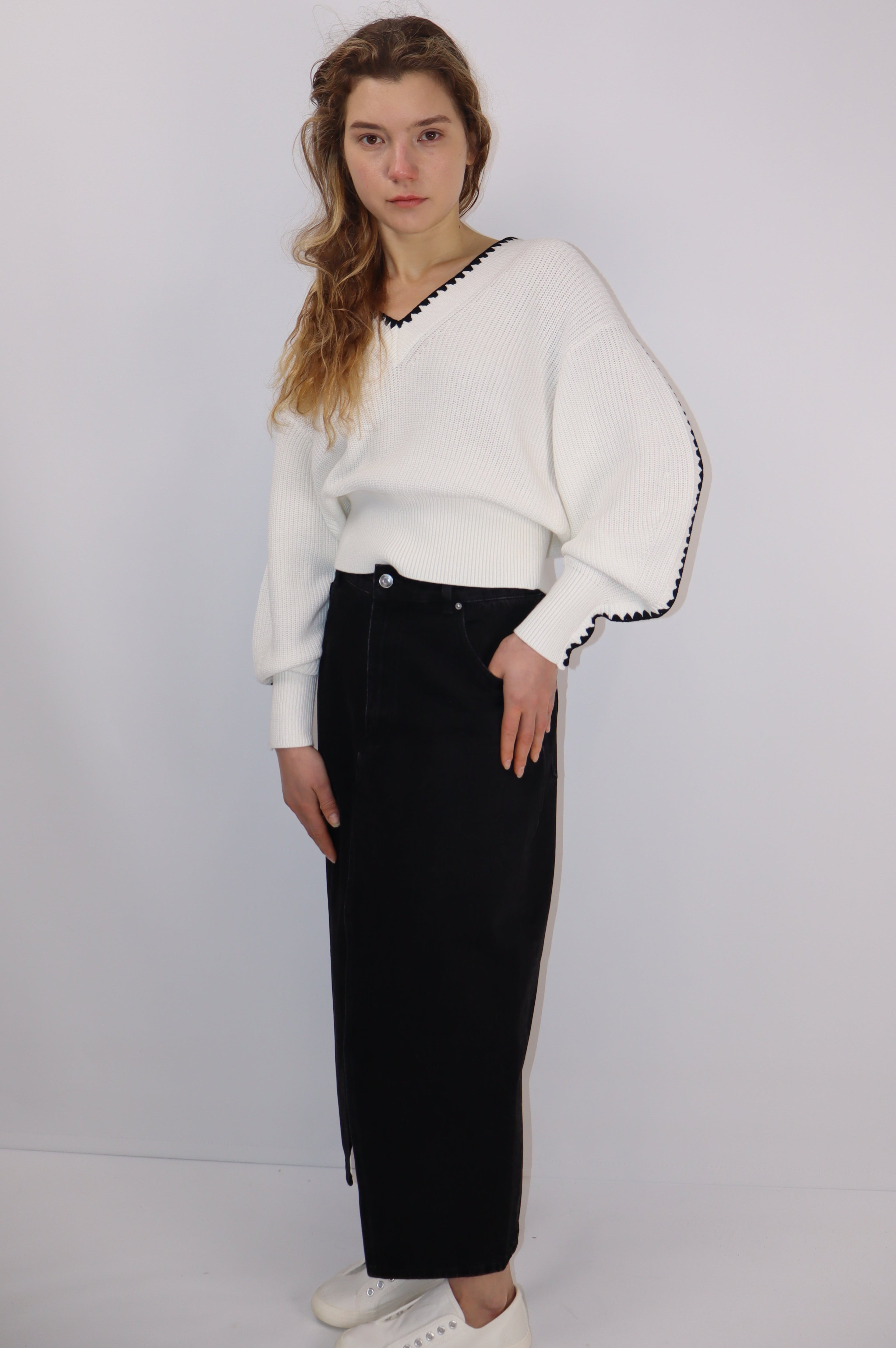 Model wearing a white linen-cotton knit sweater with black contrast trim at the V-neck and cuffs, styled with a black skirt.