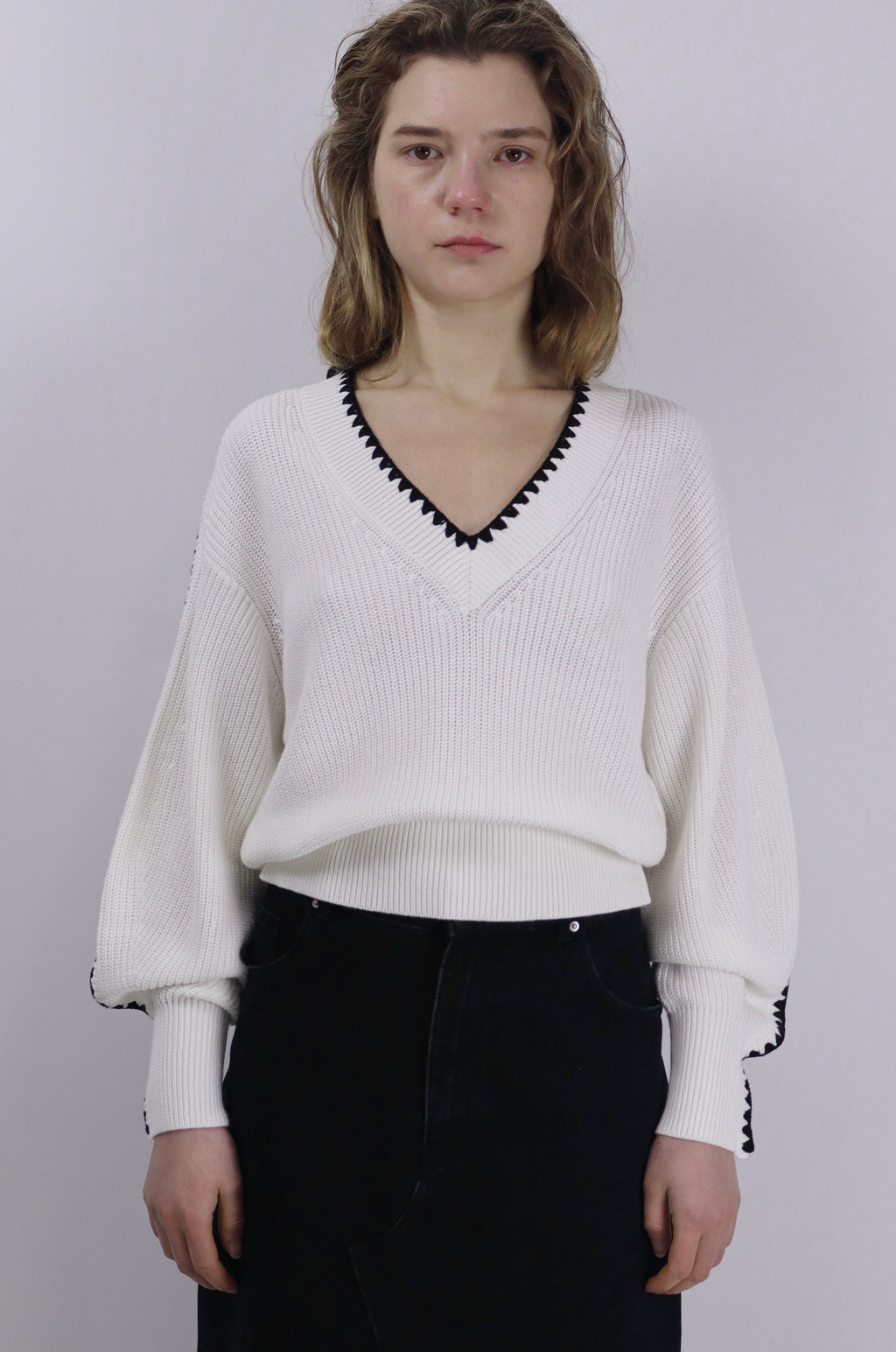 Person wearing a white linen cotton sweater with black trim on a plain background