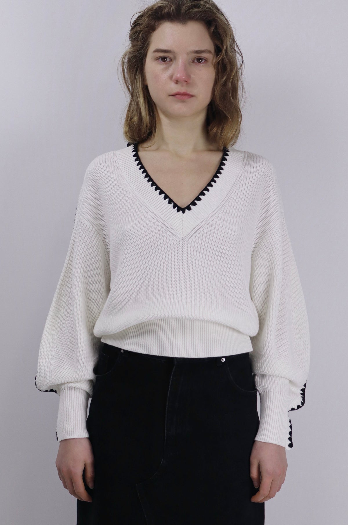 Person wearing a white linen cotton sweater with black trim on a plain background