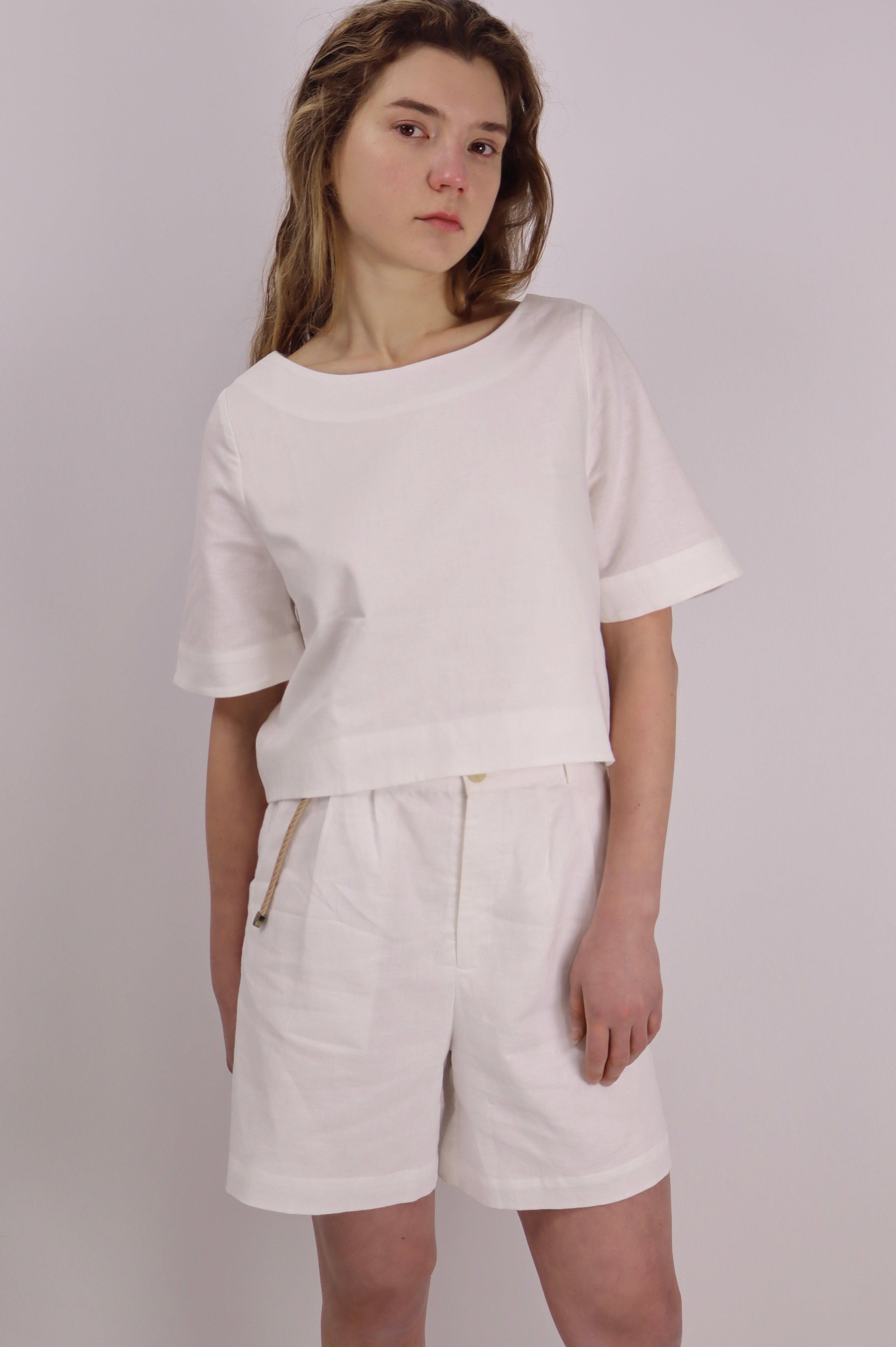 Person wearing a white linen crop top with shorts against a plain background