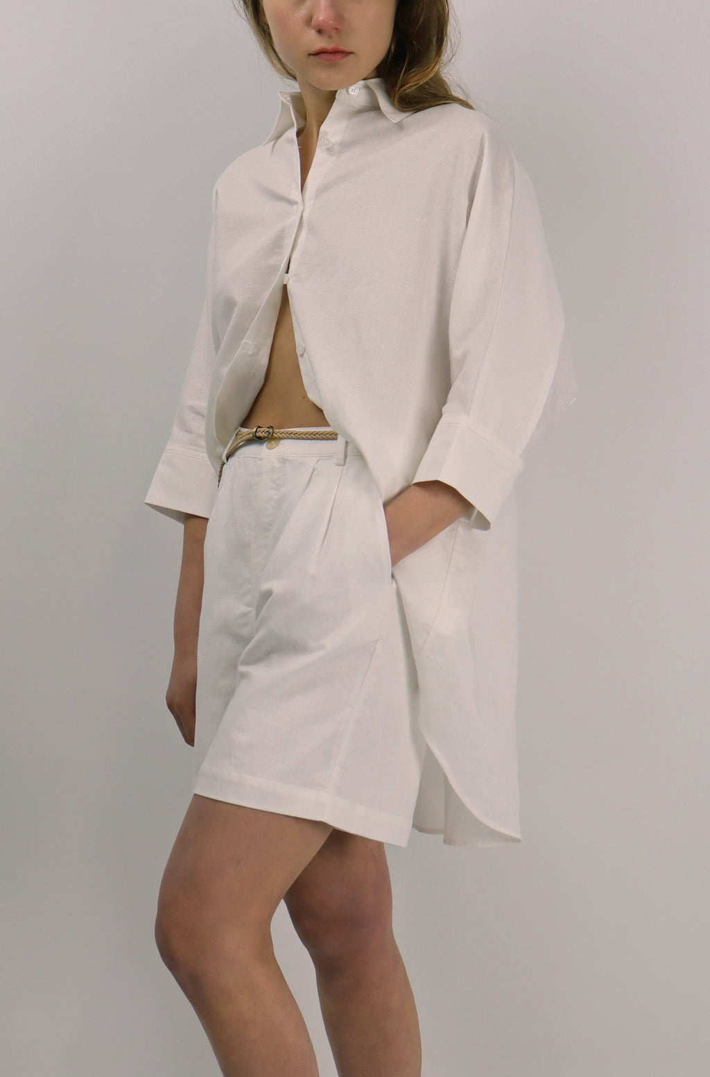 Woman wearing a white linen outfit with a jacket and skirt on a plain background
