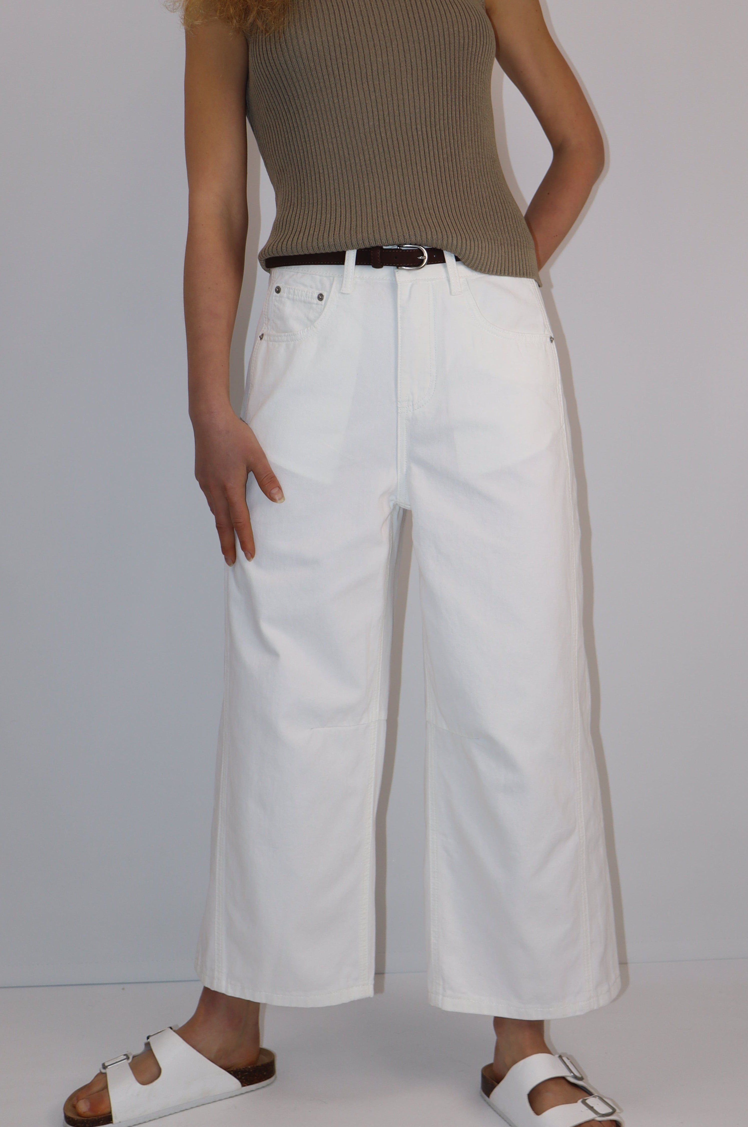 Model wearing indigo wide-leg cropped denim jeans with mid-rise waist, seam detailing at the knees, and functional pockets, paired with an off-white long-sleeve top and white sandals.
